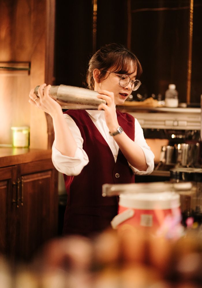 Female bartender skillfully mixing a cocktail with a shaker at an indoor bar scene.