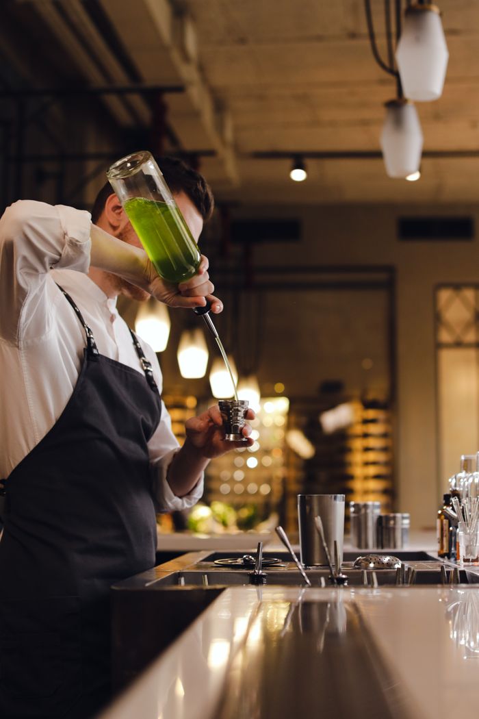 Mixologist skillfully pouring a vibrant green cocktail at a trendy bar counter.
